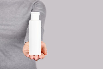 Hand with white bottle on grey background.