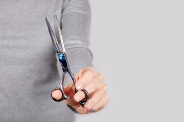 Hand with thinning scissors on grey background.