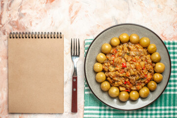 top view roasted eggplant salad and pickled plums on plate on turquoise white checkered tablecloth notebook fork on nude background