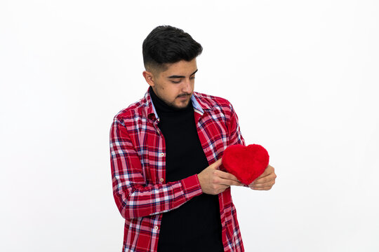 Young male holding a heart-shaped gift box in his hand. Wearing a striped shirt. Isolated image and white background.