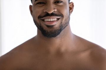 Obraz premium Close up head shot cropped image young naked african ethnicity man looking at camera, showing perfect healthy white toothy smile, satisfied with dental oral care service, feeling confident indoors.