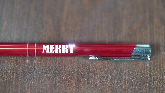 Laser engraving on metal red pen. Modern industrial technologies. Word Merry christmas