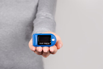 Hand with oximeter, pulse monitoring equipment on grey background.