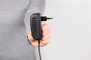 Hand with black power supply on grey background.