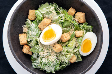 Overhead view of bowl of Caesar Salad with topped with parmesan cheese, croutons, and hard boiled egg.