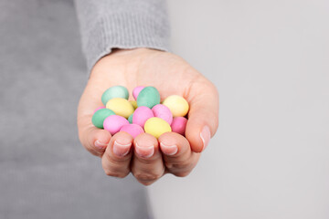 Hand with colored candies on grey background.