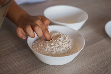 A child's hand, dipping a finger into a bowl of flour.º