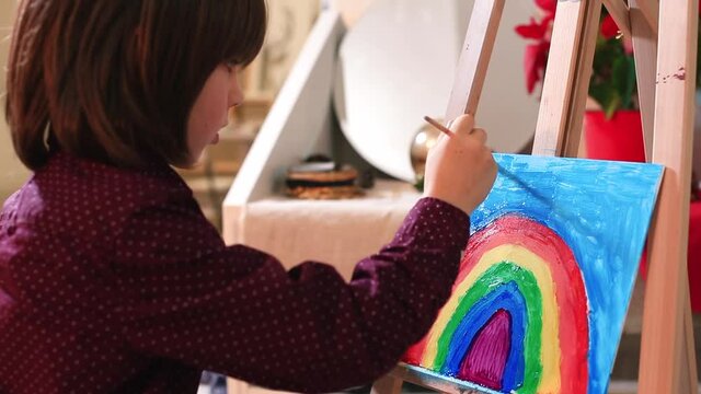 A teenager makes a painting of a rainbow on a hard surface. Dips into the palette with a brush, draws a cloud. Visualisation of children's fantasy in drawing. The pedagogical process at school.