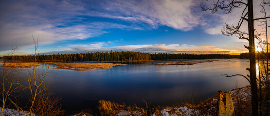 Obraz premium A panoramic view of a tranquil lake with sunbeams through the trees during a Christmas