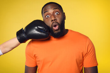Shocked black man receives a punch from somebodies. yellow background