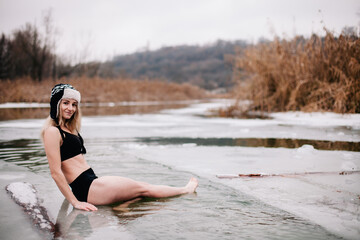 Young slender girl bathes in winter in a river hole