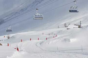 Skiing slope in the French Alpes, with skilift overhead, falling snow int hte air