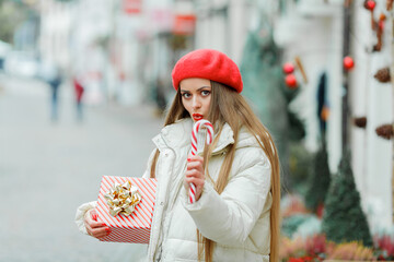 Christmas. Close-up portrait of a beautiful young woman in red biret holding a Christmas candy. Holidays.