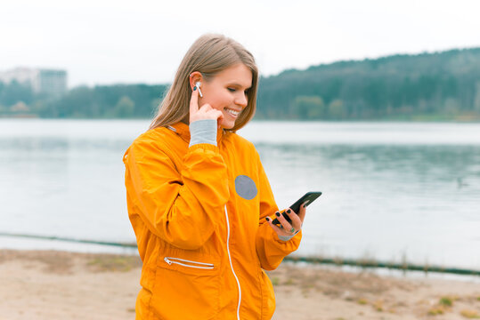 Sporty woman is walking and using her earpods and phone near a forest lake