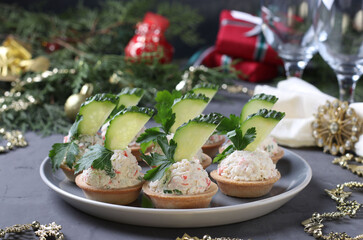 Tartlets with crab sticks, cream cheese and cucumber on a plate on grey background. Festive New Year snack. © Anzhela
