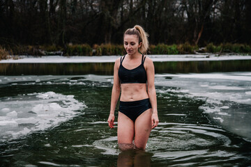 Young slender girl bathes in winter in a river hole