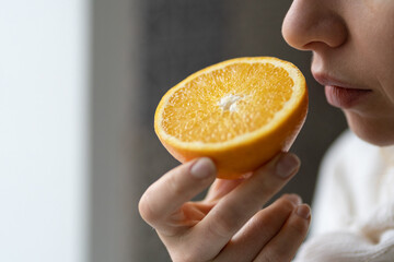 Sick woman trying to sense smell of  half fresh orange, has symptoms of Covid-19, corona virus infection - loss of smell and taste. One of the main signs of the disease.  - obrazy, fototapety, plakaty