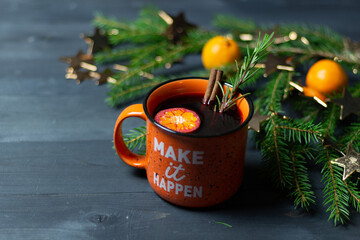 christmas still life with mulled wine in cup, tangerine, decorated with golden stars fir tree branch on black wooden background