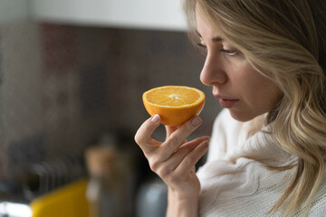 Sick woman trying to sense smell of  half fresh orange, has symptoms of Covid-19, corona virus infection - loss of smell and taste. One of the main signs of the disease.  - obrazy, fototapety, plakaty