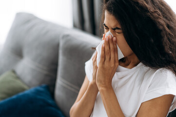 Unhealthy young woman. African american millennial girl is sick with flu, she sneezes and blows her...