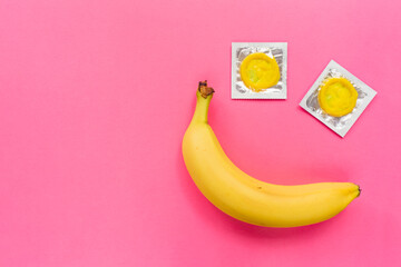 Composition with yellow condoms and banana on pink background. Safe sex and contraceptive concept....