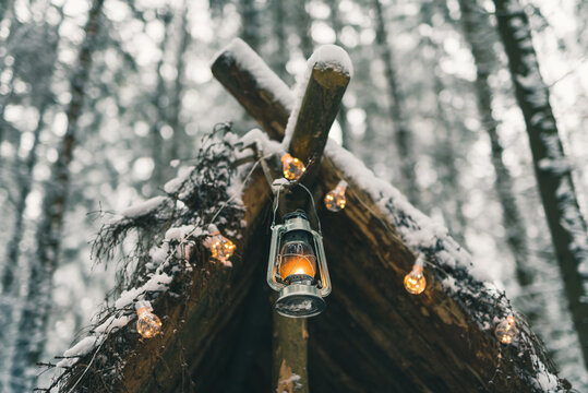 Kerosene lamp and garlands hanging on survival shelter in winter forest