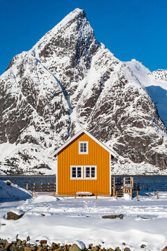 Illustrative image of a famous yellow cabin with olstind mountain in lofoten islands near to reine town on sakrisøy island. typical  spot for tourist and photography. winter norway. nice blue sky
