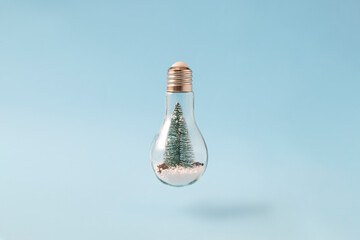 Christmas tree in a light bulb with snow on blue background. Creative minimal concept