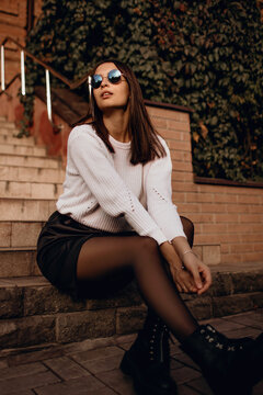 beautiful brunette girl in sunglasses sits on the steps in a skirt