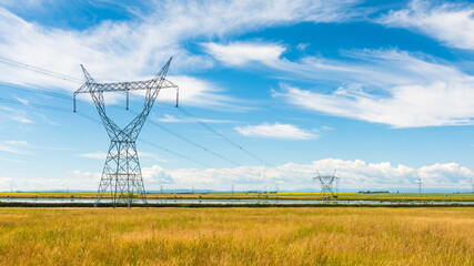 Power lines in a rural grass field. Tall steel power poles and pylons under a bright blue sky...