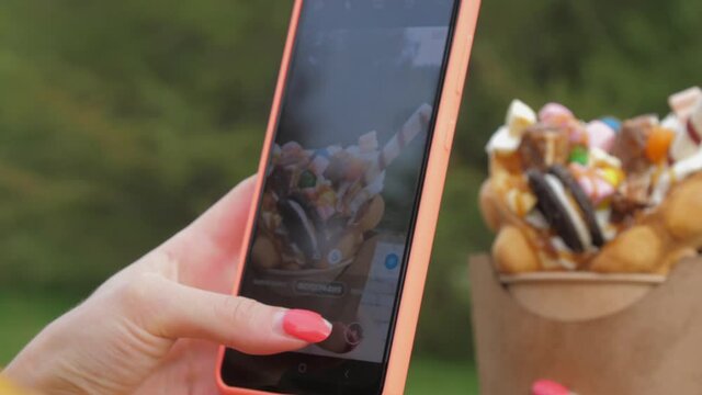 Woman takes photo of traditional Korean wafer with cream and sweets with smartphone in green park closeup. Food blog concept
