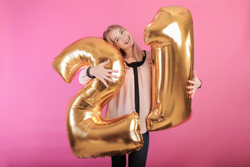 young happy girl holding large balloons in the form of number twenty one in her hands on a pink background. holiday concept