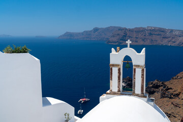 White architecture on Santorini island, Greece. Beautiful landscape with sea view. White arechers with bel and cross., blue domes in Oia village. Cliffs and see in background, selective focus