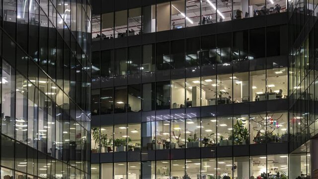 Office workers, during operation and at the end of the working day, visible through the windows of the business center, time lapse