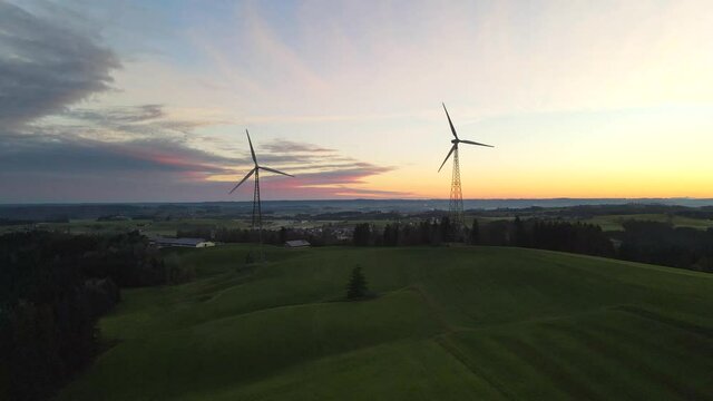 Drone shot of two wind turbine at sunrise with sun behind the blades