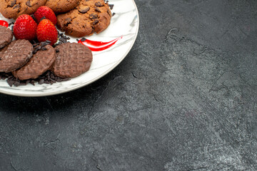half-top view tasty biscuits with pieces of chocolate and juicy strawberries with free space on a black surface