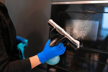 Woman washing the glass of the oven with a glass cleaner