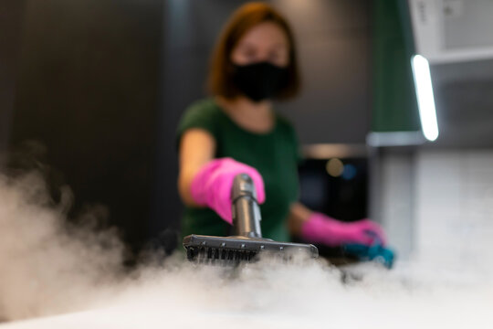 Woman employee cleaning company blows vapor out of steam generator. Steam cleaning process for kitchen furniture