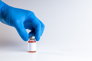 medical person holding medicine vial with red liquid and blank label over gray background. copy space. vaccine concept