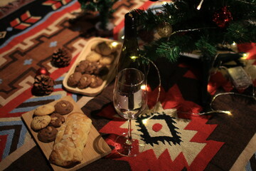 Christmas decoration with wine glass and cookies on carpet background with twinkle lights. Winter holidays, celebration and people concept.