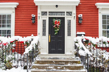 Snow covered residential stairs leading to a black door with white wood trim and windows. The stair...