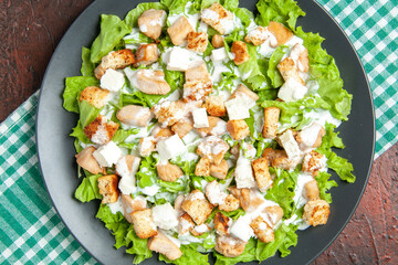 top close view caesar salad on oval plate green white checkered tablecloth on dark red background