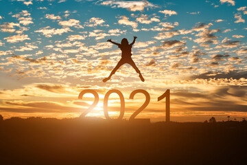 Silhouette of young woman jumping to Happy new year 2021 in sunset or sunrise background.