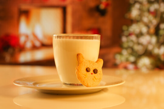 Cocoa and gingerbread cookies for New Year's Eve and Christmas themed. An image of a cat-like cookie and a glass of milk with a Christmas tree and fireplace in the background.