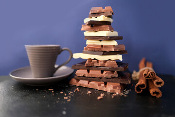 stack of broken bars of white, milk, dark chocolate on a slate board, a cup of hot cocoa, a bunch of cinnamon, the concept of sweets, a colorful meal