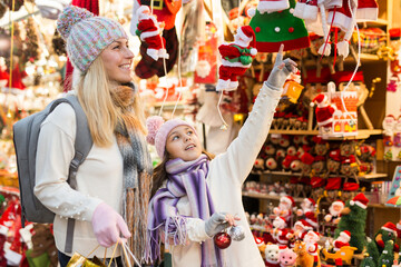 Smiling woman with tweenage daughter pointing to something while choosing decorations on traditional Christmas market