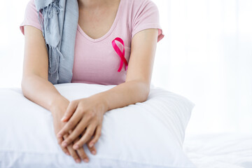 Close up of women disease mammary cancer patient with pink ribbon wearing headscarf After treatment to chemotherapy sit on bed In the bedroom at the house,healthcare,medicine concept