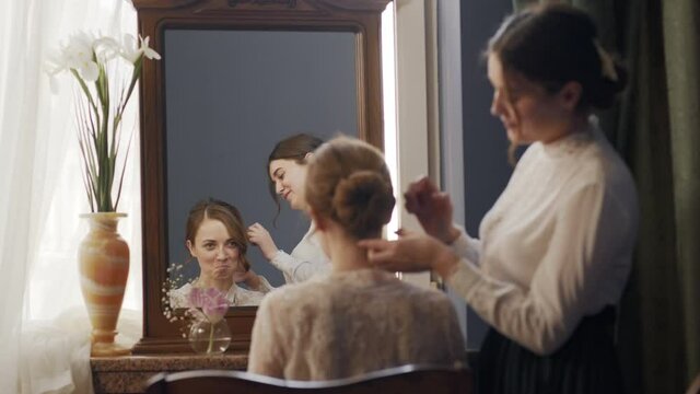 girl helps her sister to unravel her hair. Their reflection is visible in a vintage antique mirror