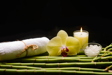 Beautiful spa setting of orchid and rolled towel 
on pile of long bamboo stem background
