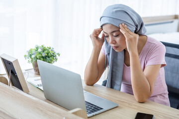 Stressed of a asian women disease mammary cancer patient Have a headaches stick pink ribbon wearing headscarf After treatment to chemotherapy with working business at laptop in office at home
